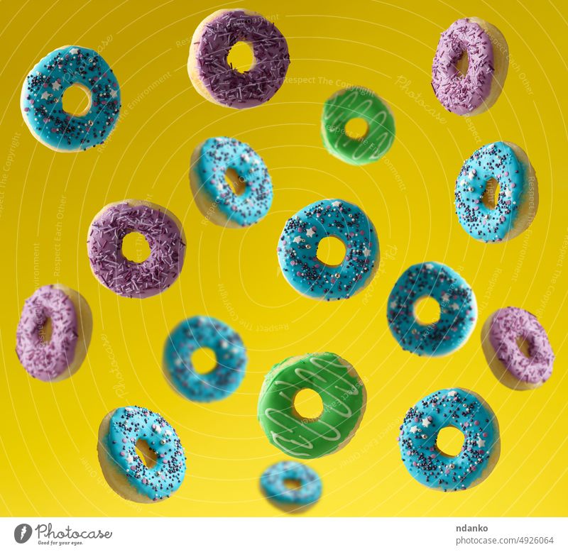 Multi-colored donuts sprinkled with sugar sprinkles fly on a yellow background dough doughnut falling food frosted glaze glazed colorful calories fried