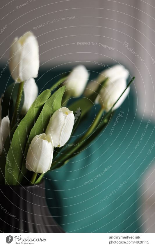 artificial white tulips and green leaves in a black vase on the table in home interior. flower beautiful blossom bouquet color plant decoration bunch colorful