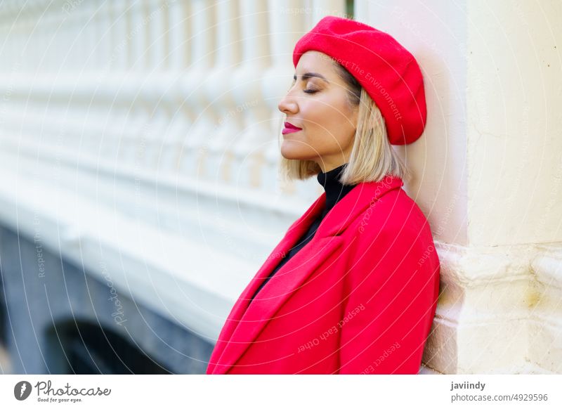 Stylish woman in red wear in city street fence style beret fashion feminine design column female outfit attractive gorgeous town blondie pillar eyes closed calm