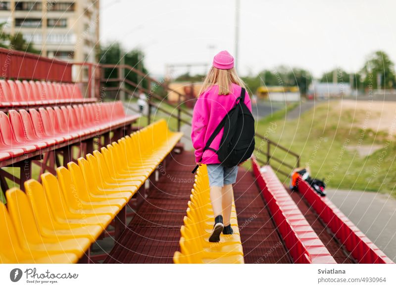 A teenage girl with a backpack walks through the stands of the school stadium. Rear view student schooltime teenager education female portrait background young