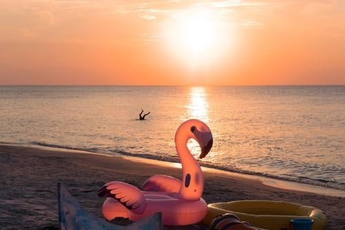 Fun on the beach. Inflatable swimming wheel toy in the shape of pink flamingo on sunset beach. Kid play in water.  Concept of summer vacation by the sea. Happy childhood magic moments.