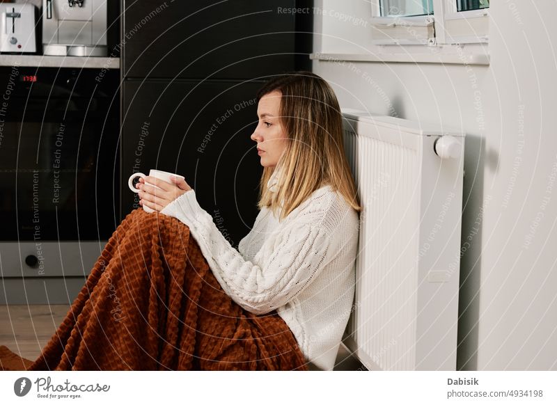 Worried woman sit near heating radiator under blanket with cup of tea gas crisis price rising costs household budget bill calculate home finance worried tax
