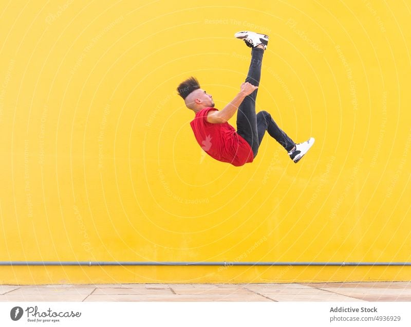 Man doing parkour trick near yellow wall man somersault stunt jump extreme city building street male urban energy flip freedom brave active upside down danger