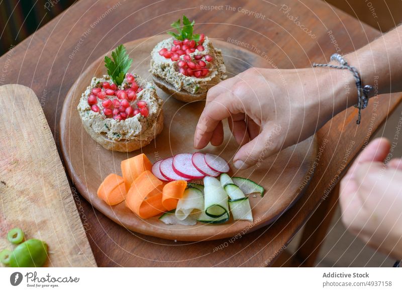 Crop person serving vegetarian food on wooden plate vegetable serve sandwich pate dish vegan bread pomegranate seed lunch parsley delicious cuisine culinary