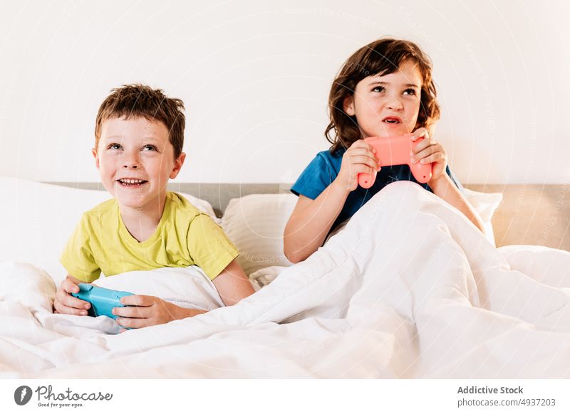 Children playing video game in bed children sibling gamepad videogame entertain amusement pastime leisure hobby focused sister concentrated brother boy girl