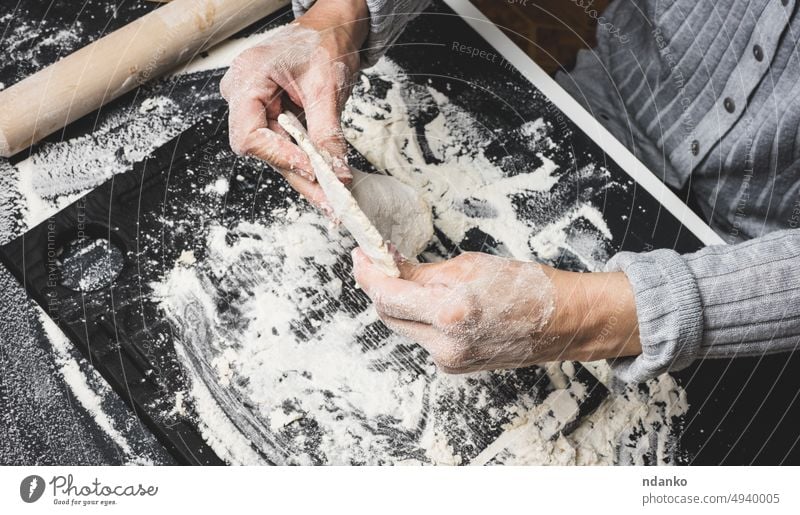 two female hands knead the dough from white wheat flour on a black table, top view cooking kitchen food bakery bread kneading ingredient preparation homemade