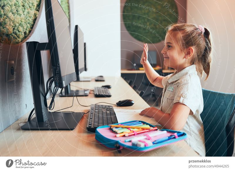 Student litttle girl having video class remotely with her teacher on computer sitting at desk in after school club at primary school. Back to school student