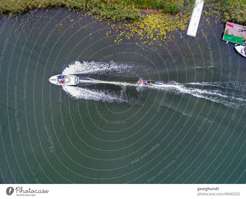 Water skiing on a lake: a motorboat pulls a water skier on the edge of a jetty Aquatics Motorboat wakeboard Lake Interior lake White crest Sports drone