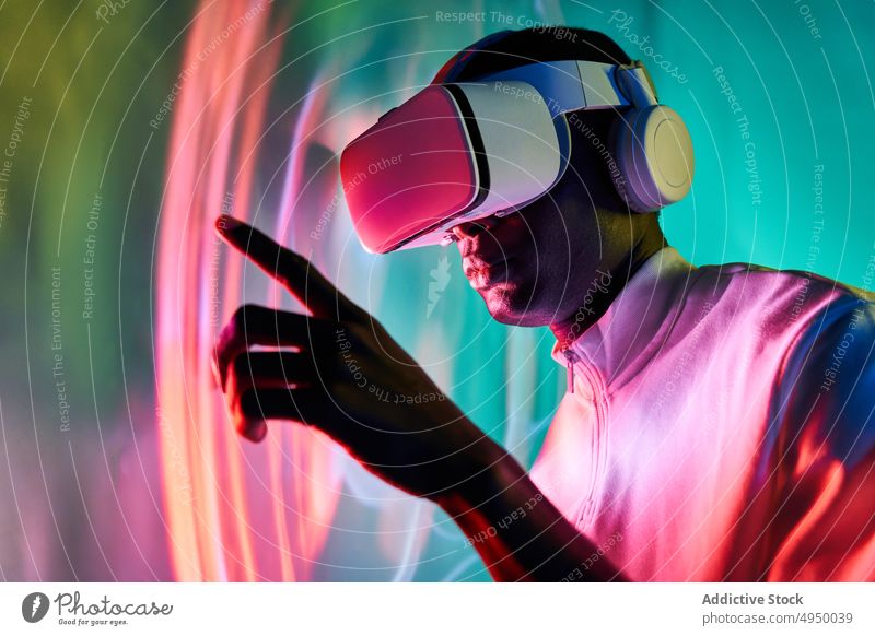 Serious black man touching large screen while exploring virtual reality in modern headset touch screen interact explore futuristic vr neon cyberspace entertain