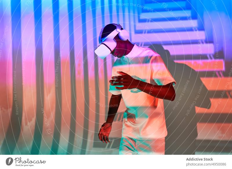 Black man looking at imaginary object while exploring cyberspace in VR glasses virtual reality dance simulator vr experience headset neon colorful immerse