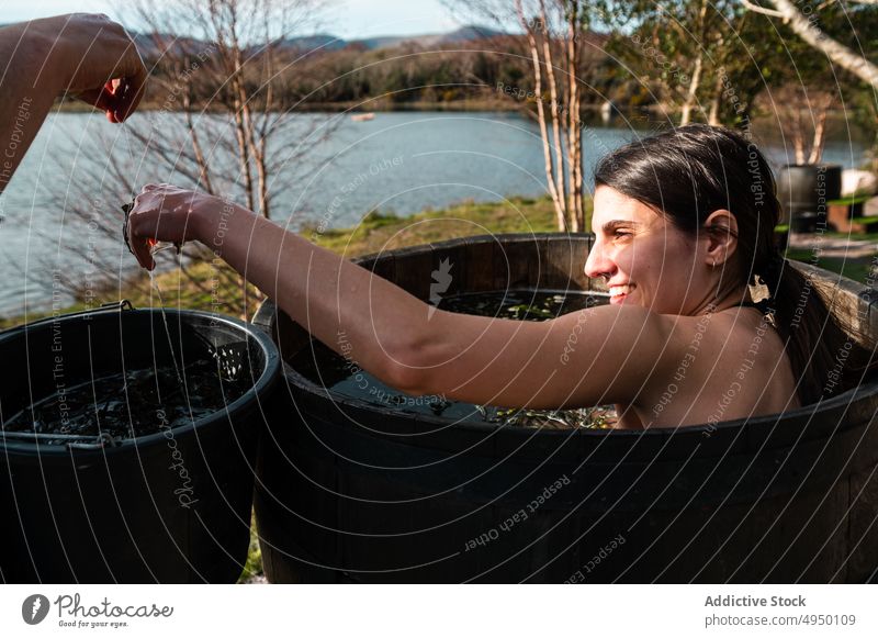 Man pouring hot water into barrel for woman bath smile lake shore algae spa happy rest tourist autumn recreation pond bucket countryside basin season service