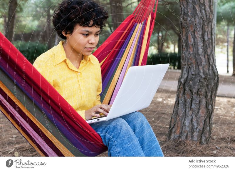 Ethnic woman with laptop in hammock teen park using rest summer relax connection surfing casual thoughtful enjoy recreation nature communicate device ethnic