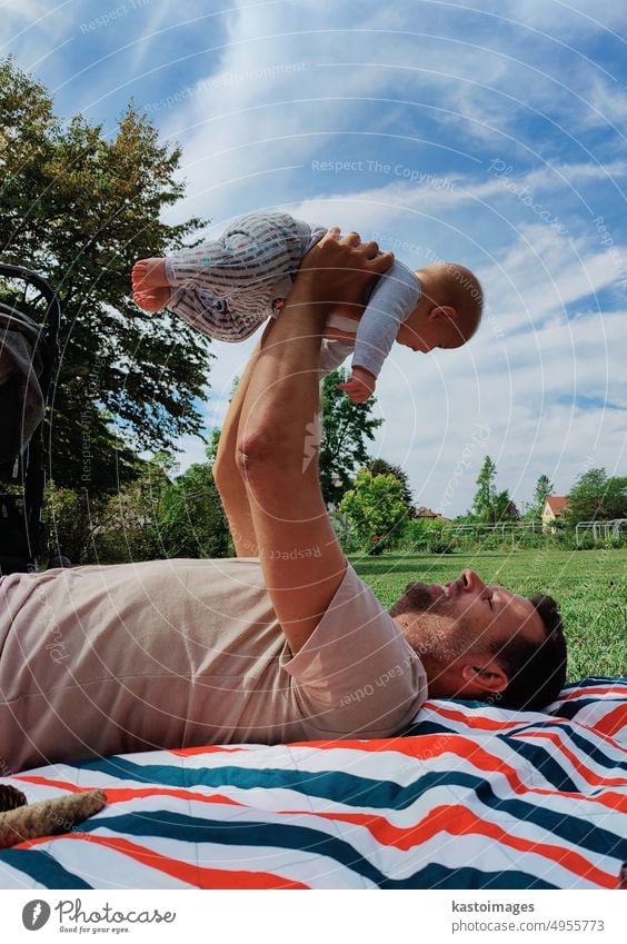 proud dad lifting and playing with his baby boy child on a mat in a meadow outdoors in public city park childhood lifestyle mom family breast happy care