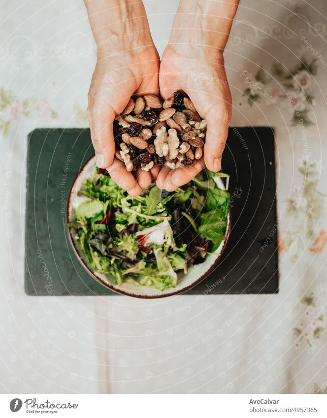Close up of hands holding up several nuts,walnut,raisin and almond above a salad bowl with lettuce.Finishing a vegan meal with nutrients,calories and proteins providing enough energy supply