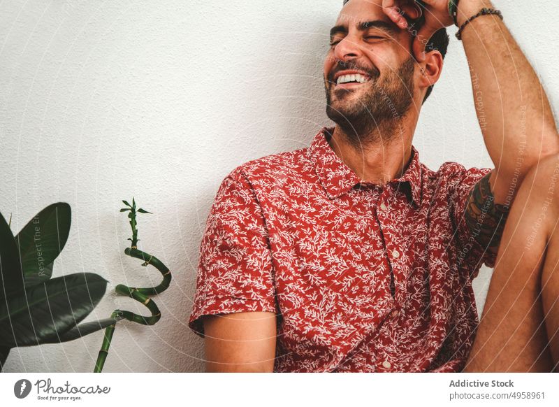 Young handsome man laughing while leaning on white wall people adult one portrait person fashion lifestyle model young beautiful attractive beauty bending
