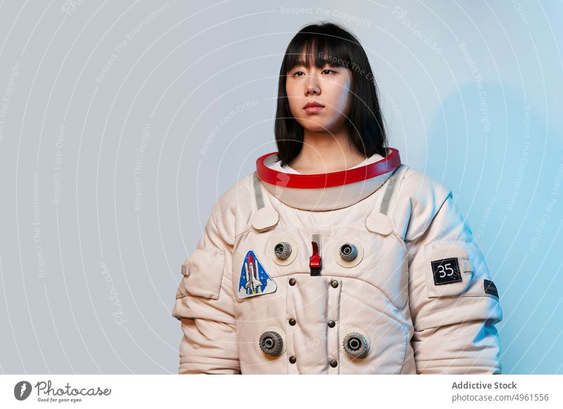 Calm Asian cosmonaut looking away woman ready mission calm serious spacesuit futuristic blue light modern female young asian chinese japanese ethnic dark hair