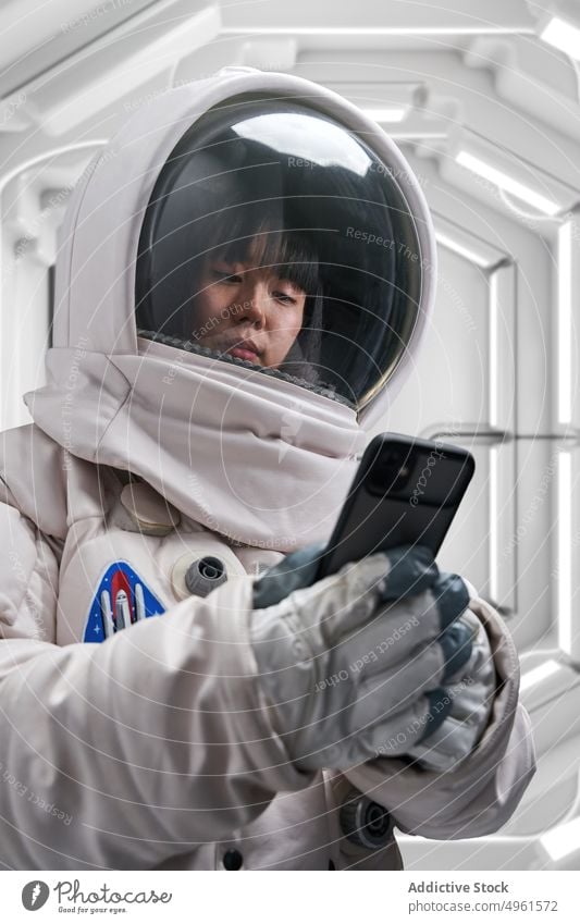 Female astronaut using smartphone inside spaceship woman spacesuit futuristic corridor science mission female young asian chinese japanese ethnic watch video