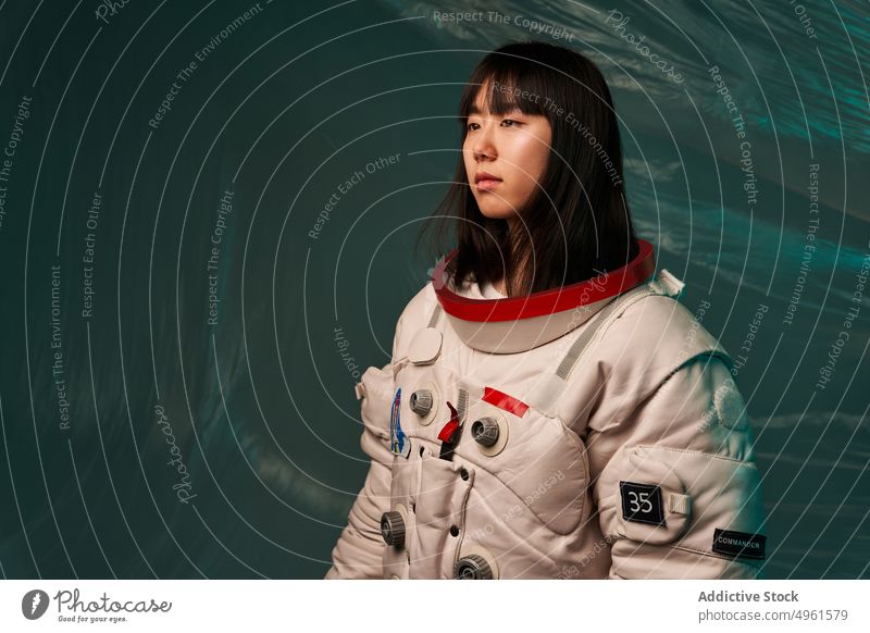 Calm Asian cosmonaut looking away woman ready mission calm serious spacesuit futuristic modern female young asian chinese japanese ethnic dark hair brunette