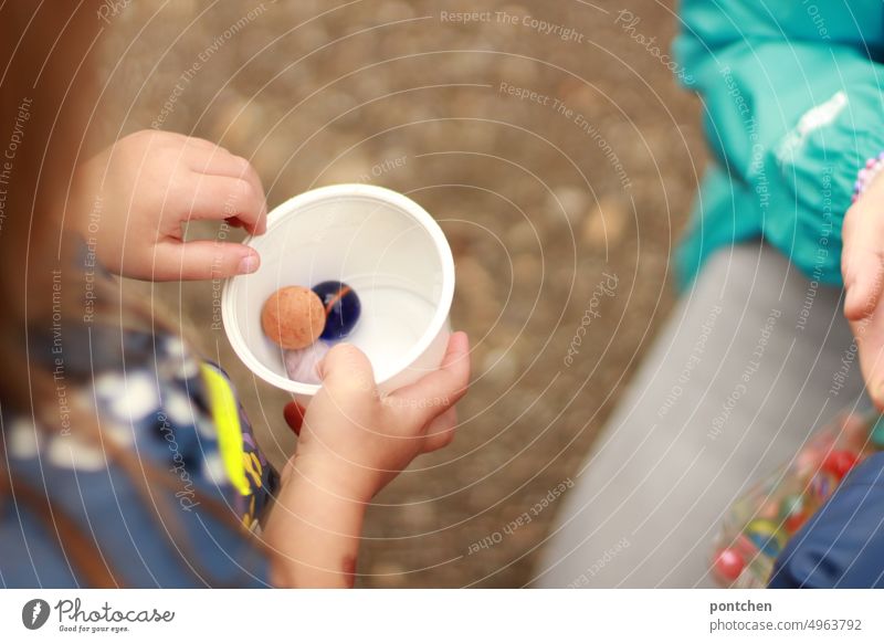 A child plays with marbles in a cup. An adult person kneels next to it. Children's game Marbles Playing Infancy joint game fun children's hands