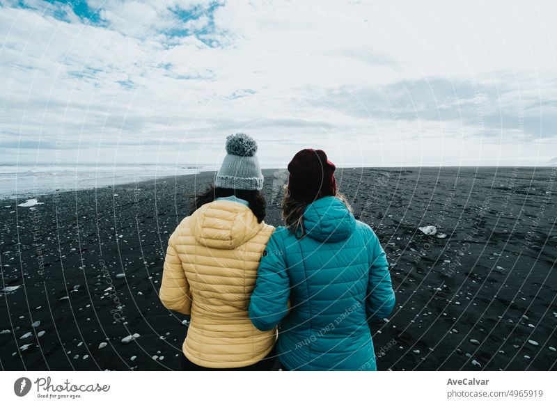 Couple female in yellow rain clothes in the black sand diamond beach near Jokulsarlon during a road trip travel exploring wild lands of Iceland.Adventure vacations healthy lifestyle backpacking