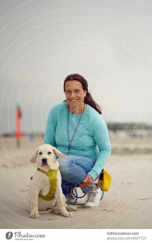 Attractive smiling woman posing with her puppy at the beach kneeling on the sand with copy space above dog adorable labrador retriever blond sitting