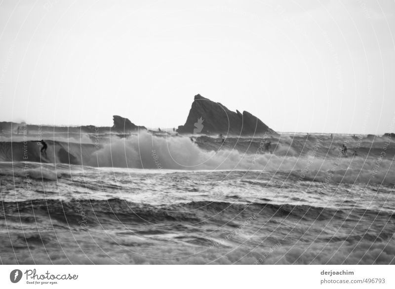 In the whipped up sea surfers are on the way. In the background there is a rock in the water.wave surfers Joy Athletic Senses Swimming & Bathing