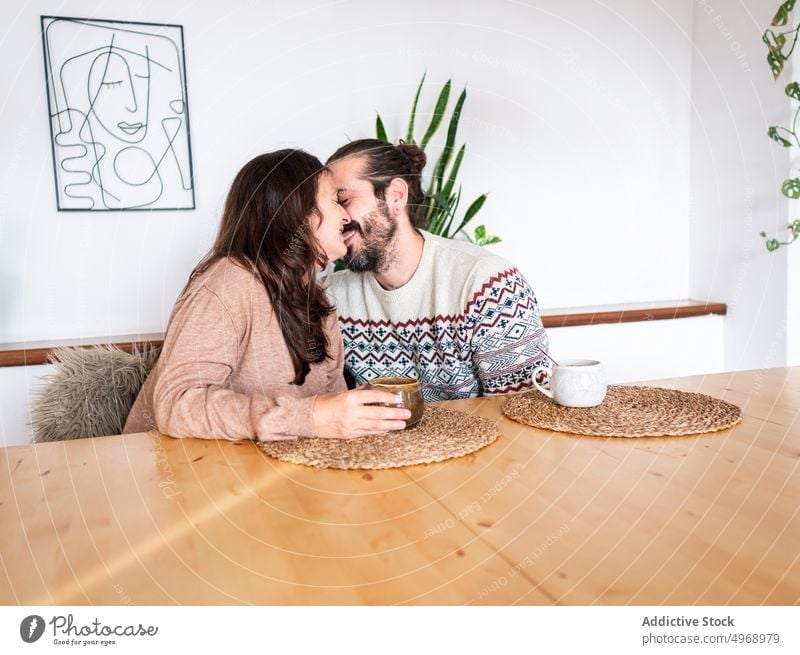 Couple kissing while sitting at table couple relationship love coffee cup home happy together man woman romantic affection young tender passion apartment date