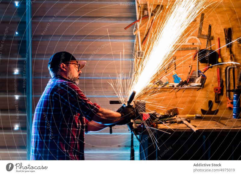 Male cutting piece of metal in modern workshop man angle grinder spark worker equipment using workplace instrument mechanic craftsman process industry garage