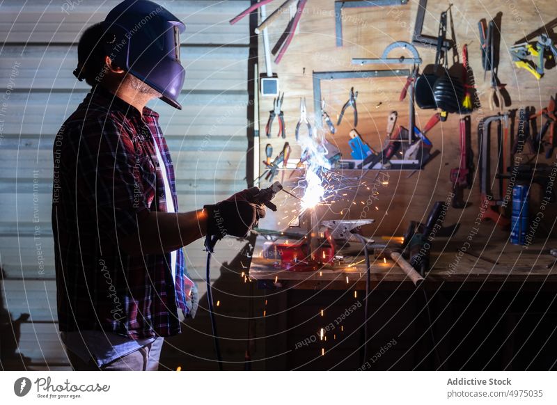 Male cutting piece of metal in modern workshop man angle grinder helmet spark worker equipment using workplace instrument mechanic craftsman process industry
