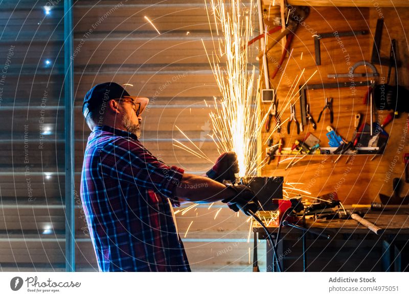 Male cutting piece of metal in modern workshop man angle grinder spark worker equipment using workplace instrument mechanic craftsman process industry garage
