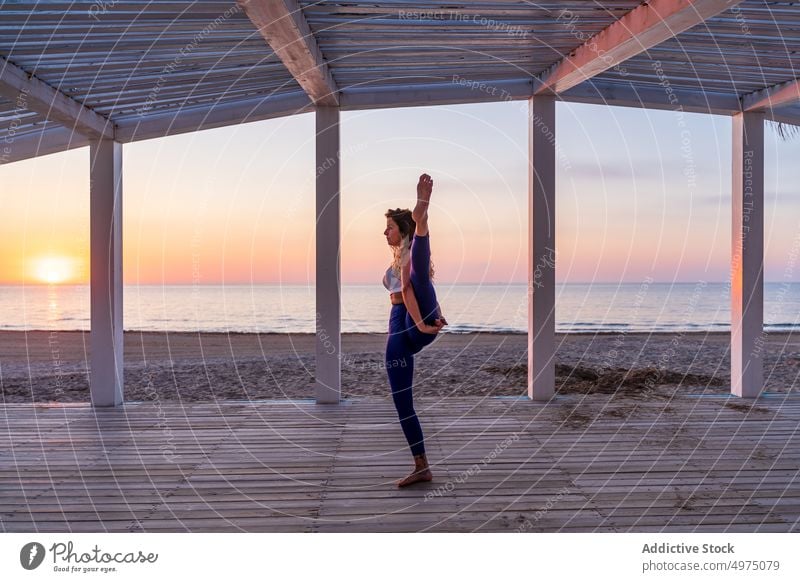 Flexible woman doing yoga at seaside during sunrise pose terrace tranquil sportswear practice wooden anjaneyasana serene healthy harmony calm dawn peaceful