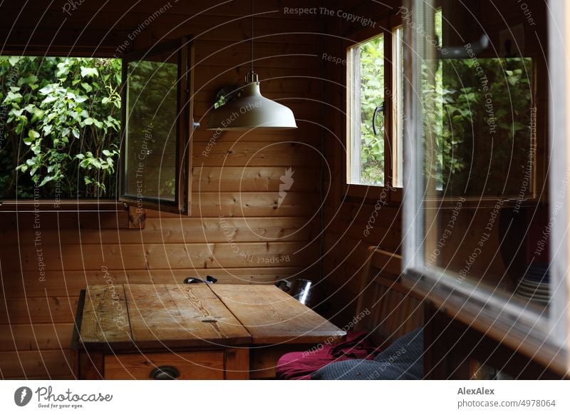 View through open window into wooden garden hut with wooden table, bench and other windows. Arbour Garden shed Hut bungalow Table Lamp light Suspension lamp