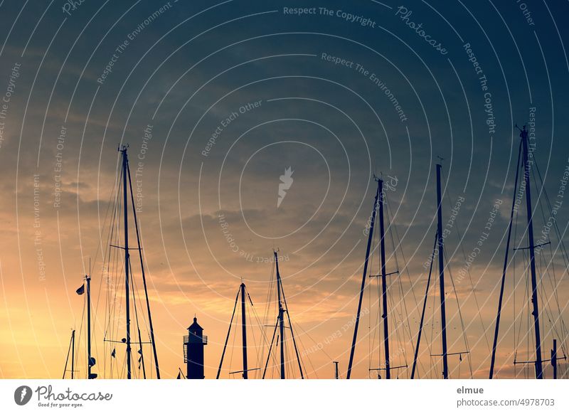 View of masts of sailboats and a lighthouse at sunrise / marina sailing yacht Lighthouse Sunrise Sailing masts morning mood Navigation Sport shipping
