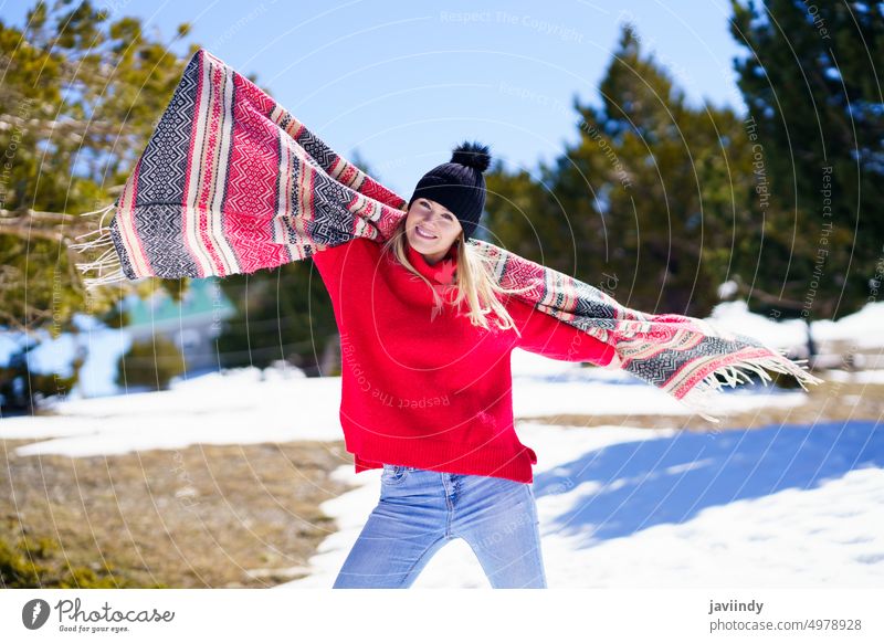 Happy young blonde woman waving her scarf in the wind in a forest in the snowy mountains. winter girl joy smile warm white cheerful clothes fun happy outdoor