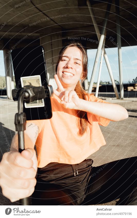 Portrait of young woman content maker starting and recording a shooting greeting with big smile on social network.Holding mobile phone and doing peace symbol checking everything is ok. Casual stream