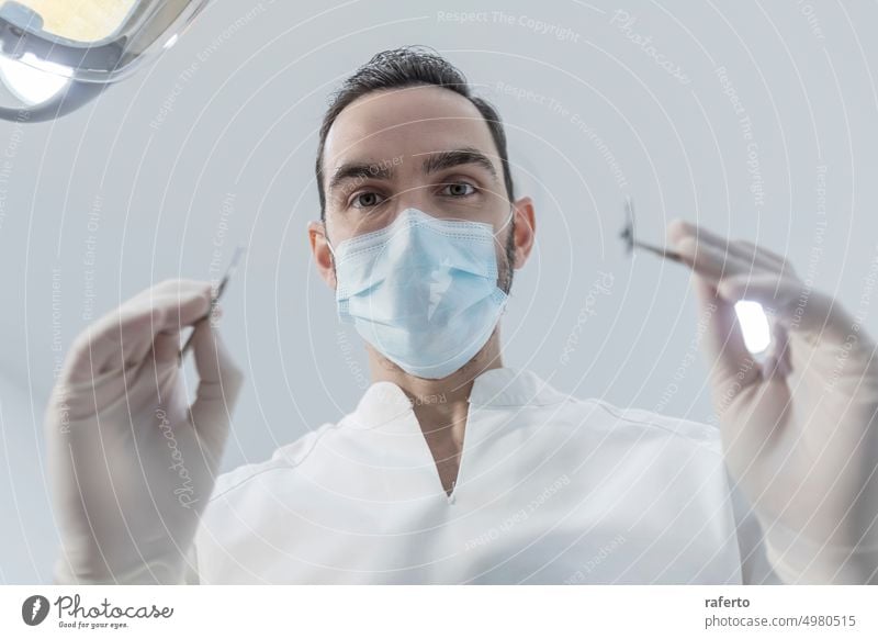 Low angle view of male dentist in medical mask holding dentist tools for dental procedure in clinic Dentist person stomatology dentistry low angle glove closeup