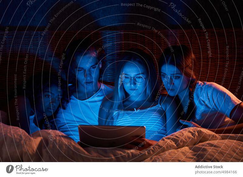 Scared flatmates watching horrors in dark bedroom friend scary tablet night frighten movie lying together gadget device using evening sleepwear fear video