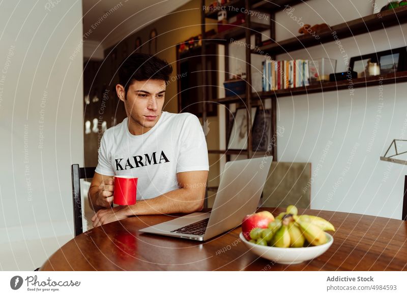 Young man drinking coffee and working on computer at home handsome young male caucasian lifestyle morning indoor focus happy cup tea laptop table living room