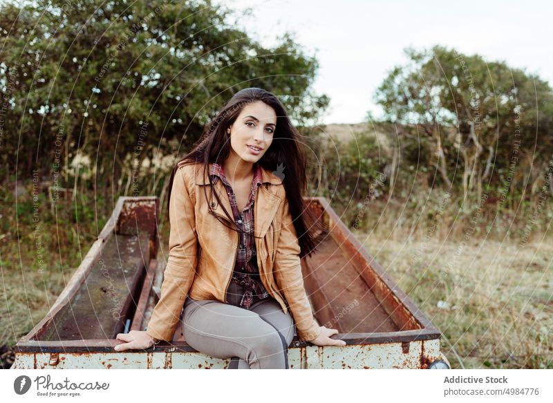 Charming woman sitting on rusty wagon in countryside cheerful rural style modern posture nature trendy landscape tranquil exterior aged alone farm agriculture