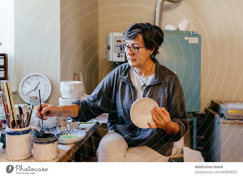 Mature craftswoman painting ceramic bowl pottery clay brush artisan handicraft create handmade master workshop skill process small business female mature