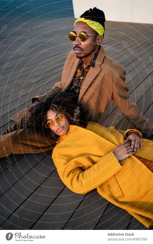 Sensual fashionable couple on wooden floor trendy colorful love caress together dream ethnic black african american afro dreadlocks coat autumn cuddle harmony