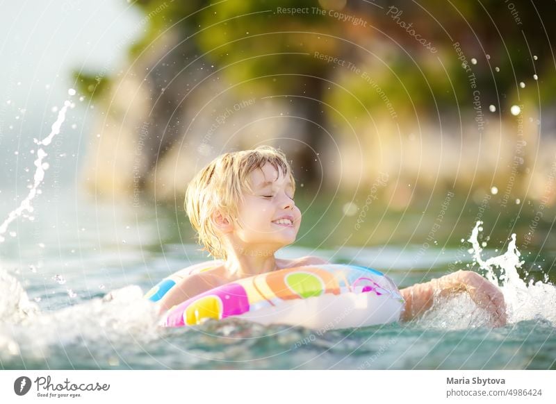 Little boy swimming with colorful floating ring in sea on sunny summer day. Cute child playing on beach. Family and children's resort holiday during summer vacations.