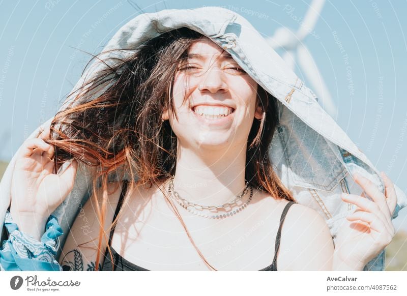 Close up portrait of a happy young woman covering head with jacket sunny day 20s smiling chatting eye friendly journey joyful laughing listen look mood music