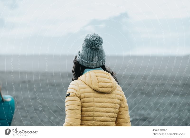 Woman on the black sand beach in Iceland, winter clothes.Shot from behind.Travel to iceland concept. woman rock desert person island ocean south alone balance