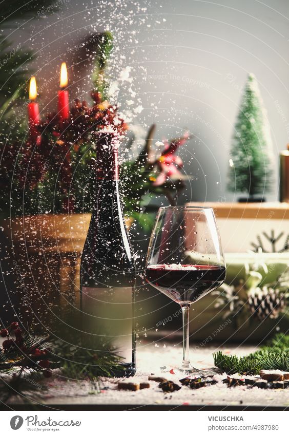 Christmas red wine glass and bottle on table with candles, holiday decorations, gift boxes and falling snow christmas wine bottle shiny design winter