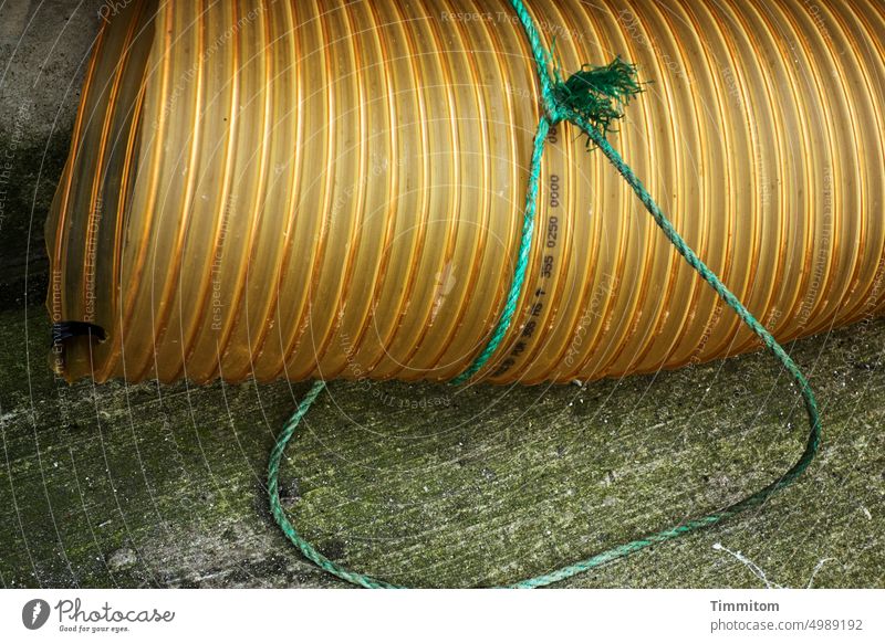 Thick tube on a long leash conduit Plastic Yellow Opening String Green Knot Concrete floor Colour photo Deserted Rope Harbour Denmark