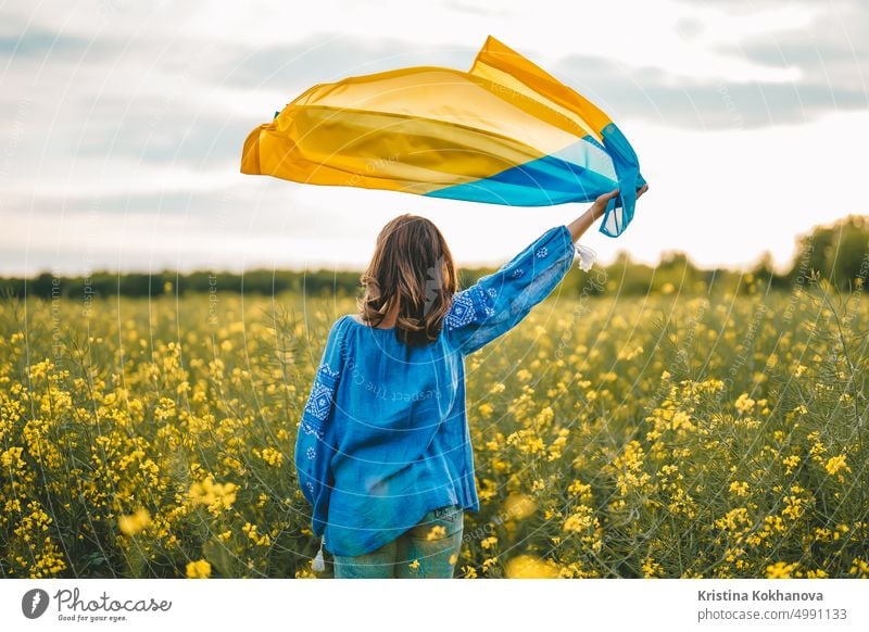 Ukrainian patriot woman waving national flag in canola yellow field. Rare, back view. Ukraine unbreakable, peace, independence, freedom, victory in war.
