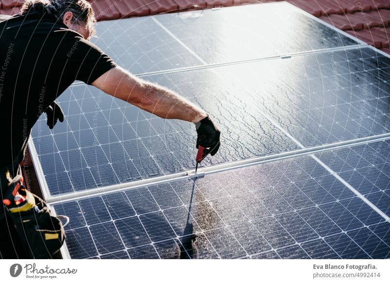 mature Technician man assembling solar panels on house roof for self consumption energy. Renewable energies concept green energy technician photovoltaic tools