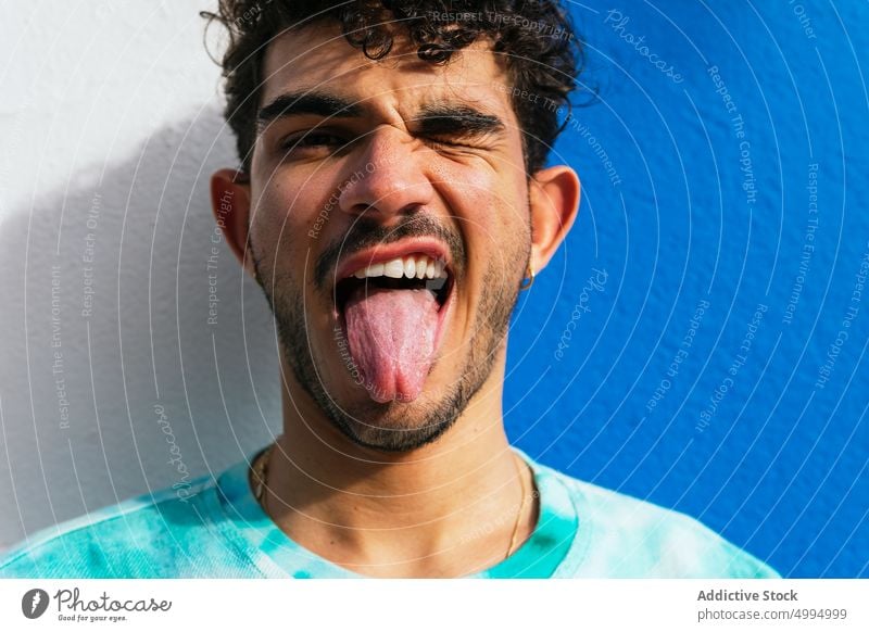 Funny Hispanic man showing tongue show tongue playful wink grimace funny wall urban street portrait male tongue out make face hispanic ethnic young adult