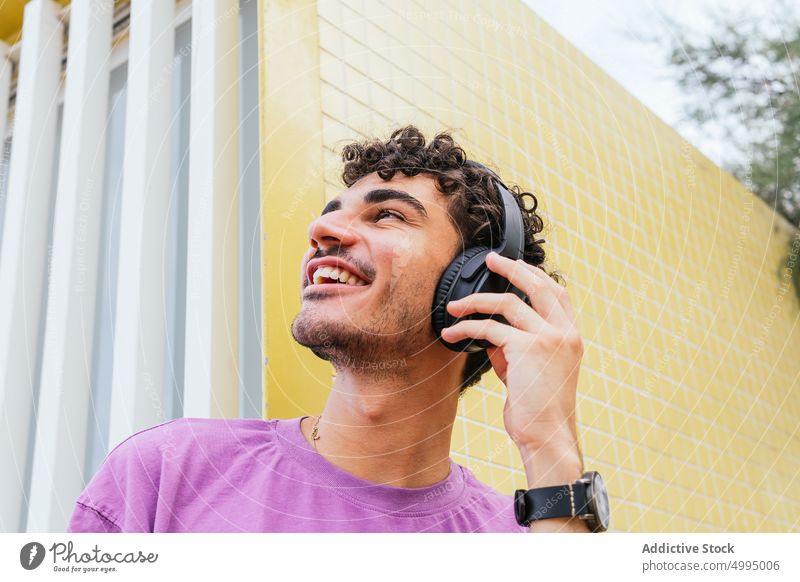 Hispanic meloman listening to music on beach adjust headphones enjoy smile weekend male hispanic ethnic young wall tile street summer song sound optimist bright